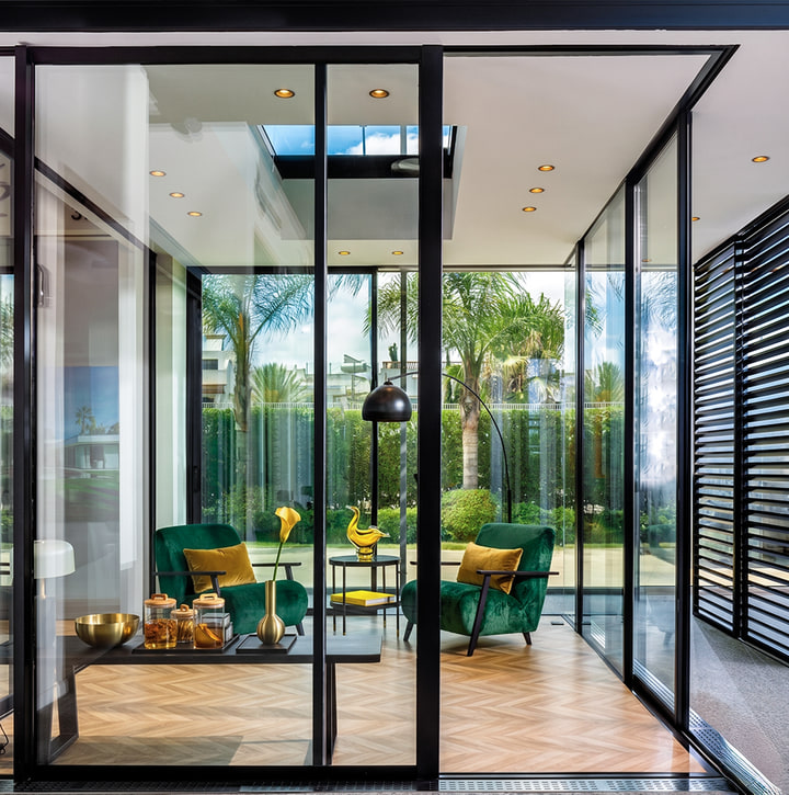 Salon design encadré par des cloisons en aluminium noir mat et une baie vitrée donnant sur les palmiers — réalisation Aluminium Tanger